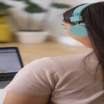 Pessoa conectada em chamada de vídeo com fones de ouvido coloridos, em ambiente doméstico