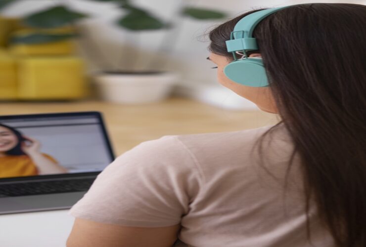 Pessoa conectada em chamada de vídeo com fones de ouvido coloridos, em ambiente doméstico