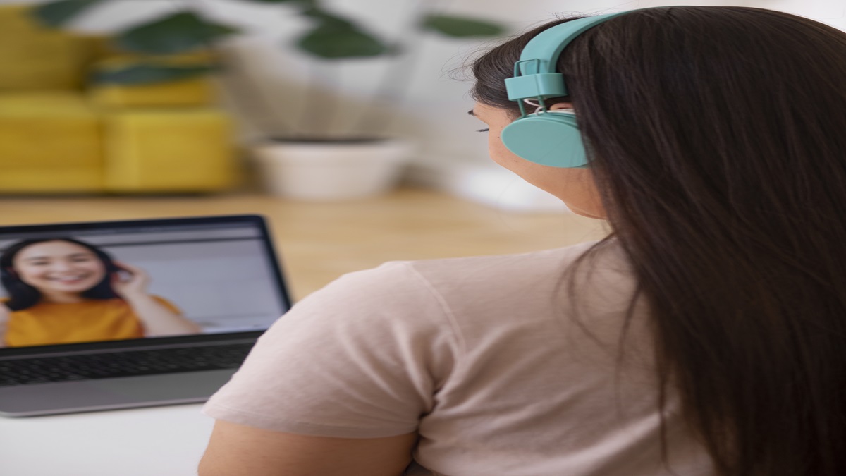 Pessoa conectada em chamada de vídeo com fones de ouvido coloridos, em ambiente doméstico